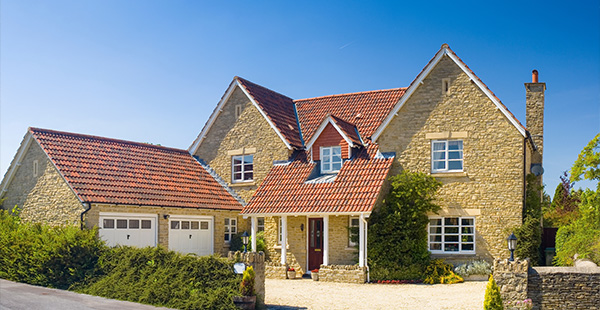 stone house with red roof greenery two garage doors sunny day